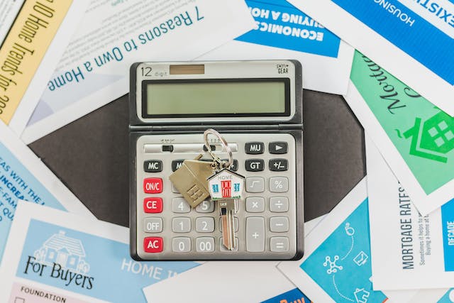 house keys on a calculator surrounded by home purchasing documents